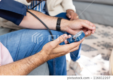 Checking blood pressure, man holding sphygmomanometer with senior couple sitting 116812207