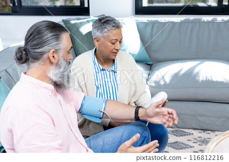 Checking blood pressure, senior couple sitting on couch in living room Checking blood pressure, senior couple sitting on couch in living room 116812216