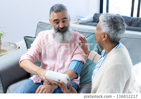 Checking blood pressure, senior man sitting on couch with woman assisting Checking blood pressure, senior man sitting on couch with woman assisting 116812217