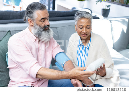 Checking blood pressure, senior couple sitting on couch, focusing on health Checking blood pressure, senior couple sitting on couch, focusing on health 116812218