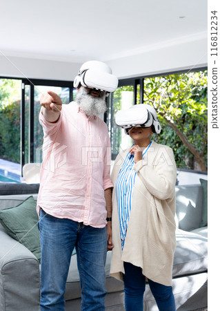 Using VR headsets, senior couple exploring virtual reality in living room 116812234