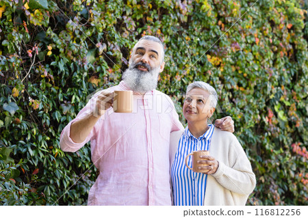 Enjoying coffee together, senior couple standing outdoors and smiling 116812256