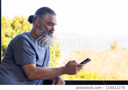 Senior man using smartphone while leaning on balcony railing, enjoying outdoors, copy space Senior man using smartphone while leaning on balcony railing, enjoying outdoors, copy space 116812278