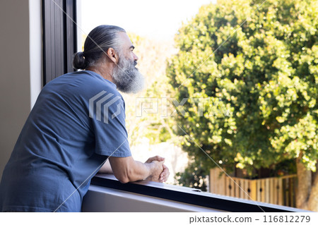 Senior man leaning on windowsill, looking outside at trees, enjoying view, copy space 116812279
