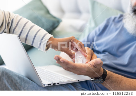Handing pills to senior man using laptop, receiving medication at home 116812288