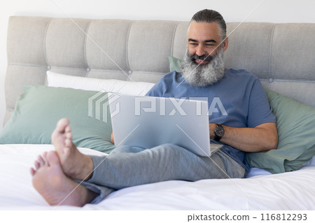Working from home, senior man using laptop while sitting on bed 116812293