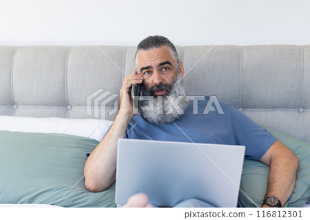 Using laptop and talking on smartphone, man working from home on bed 116812301