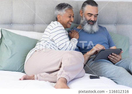 Senior couple relaxing on bed, using tablet and smiling together Senior couple relaxing on bed, using tablet and smiling together 116812316