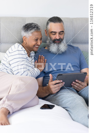 Senior couple relaxing on bed, using tablet and smiling together Senior couple relaxing on bed, using tablet and smiling together 116812319