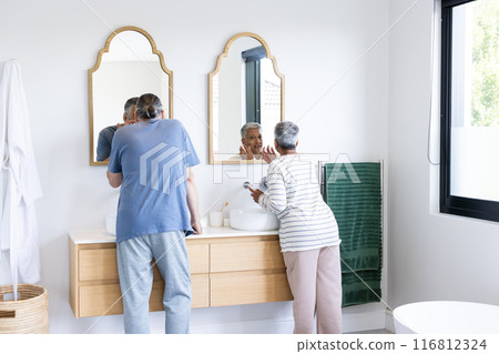 Brushing teeth, senior couple standing at bathroom sink, enjoying morning routine 116812324
