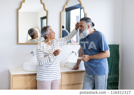 Senior couple in bathroom, woman applying cream to man's face, smiling together Senior couple in bathroom, woman applying cream to man's face, smiling together 116812327