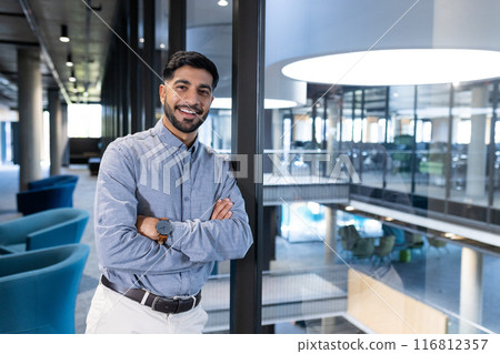 Smiling businessman in modern office, standing with arms crossed confidently, copy space Smiling businessman in modern office, standing with arms crossed confidently, copy space 116812357