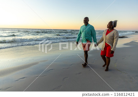 Senior African American couple enjoys a beach stroll at sunset Senior African American couple enjoys a beach stroll at sunset 116812421
