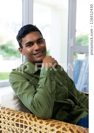 Young biracial man smiles while seated indoors, with copy space 116812430