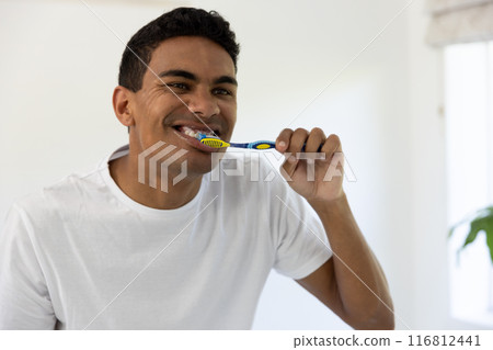 Young biracial man brushing teeth in a bright home bathroom Young biracial man brushing teeth in a bright home bathroom 116812441