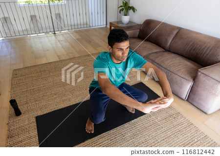 Young biracial man exercises on a yoga mat at home Young biracial man exercises on a yoga mat at home 116812442