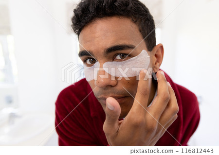 Young biracial man applies skincare products at home 116812443