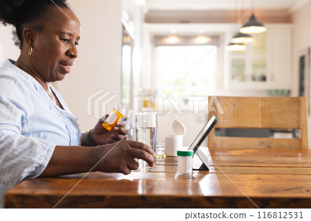 Sad senior african american woman taking pills and using tablet at home Sad senior african american woman taking pills and using tablet at home 116812531