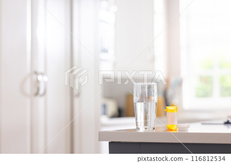 Close up of box of pills and glass of water on table in white kitchen 116812534