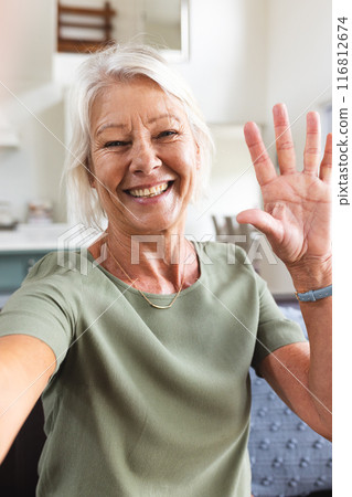 Vertical of happy senior caucasian woman having video call, smiling and waving in living room 116812674