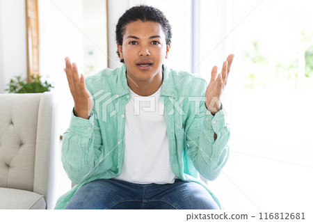 Young biracial man gestures while talking on a video call in a bright home setting 116812681