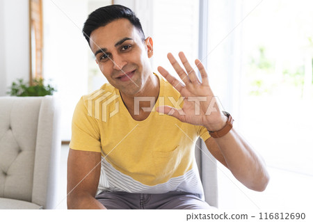 Middle Eastern man greets warmly from a bright home setting during a video call 116812690