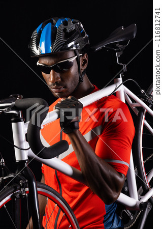 African American cyclist poses with his bike on a black background, with copy space African American cyclist poses with his bike on a black background, with copy space 116812741