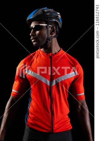 African American cyclist poses confidently on a black background, with copy space African American cyclist poses confidently on a black background, with copy space 116812743