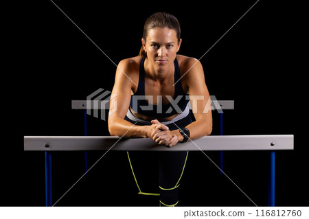 Female athlete shows strength and focus overcoming hurdles at gym. 116812760