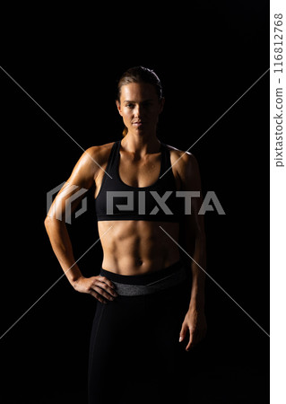 Young Caucasian female athlete poses confidently in a fitness setting on a black background 116812768