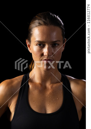 Determined young Caucasian female athlete stands ready for a workout on a black background 116812774