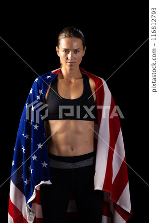 Athletic young Caucasian female athlete draped in an American flag on a black background 116812793