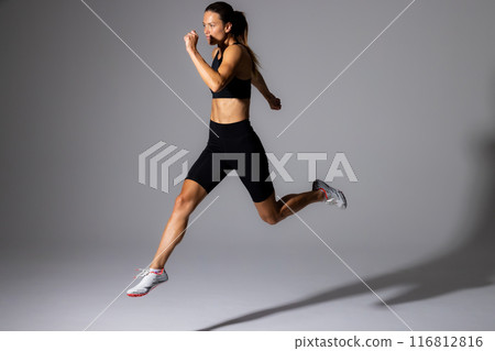 Young Caucasian female athlete in mid-stride during an indoor run on a white background 116812816