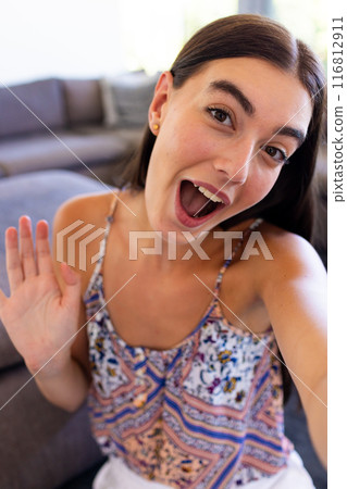 Teenage Caucasian girl greets enthusiastically from a cozy home setting Teenage Caucasian girl greets enthusiastically from a cozy home setting 116812911