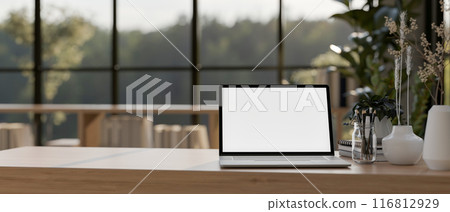 A laptop computer with a white-screen mockup on a wooden table in a contemporary room. 116812929