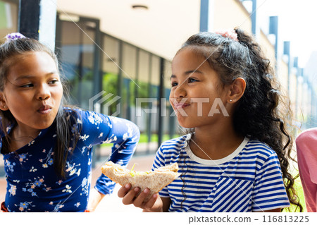 In a school setting, a young Hispanic girl enjoys a slice of pizza 116813225