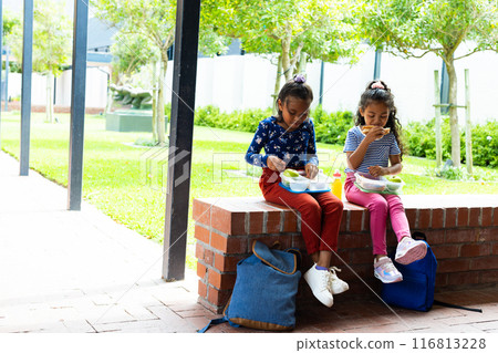 In a school courtyard, two young Hispanic girls enjoy a lunch break, copy space In a school courtyard, two young Hispanic girls enjoy a lunch break, copy space 116813228