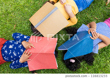 Three children lie on the grass with colorful books covering their faces in school 116813233