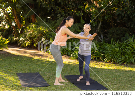 Practicing yoga outdoors, young asian woman assisting elderly asian woman on yoga mats 116813333