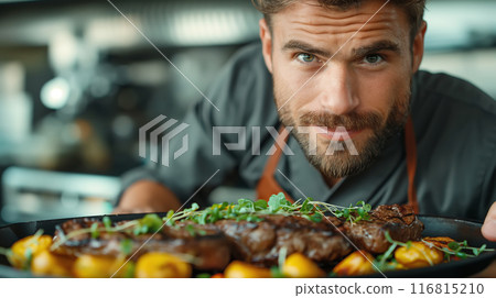 A chef presents gourmet steak dish garnished with fresh herbs, embodying fine dining 116815210