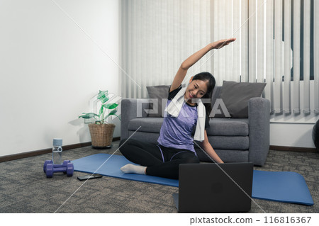 Asian woman stretching during a yoga class with a trainer at her laptop computer at home. 116816367