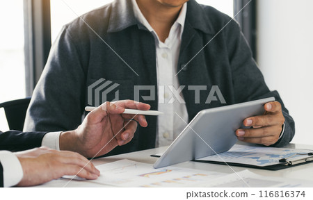 Business partnership coworkers using a tablet to chart company financial statements report and profits work progress and planning in office room. 116816374