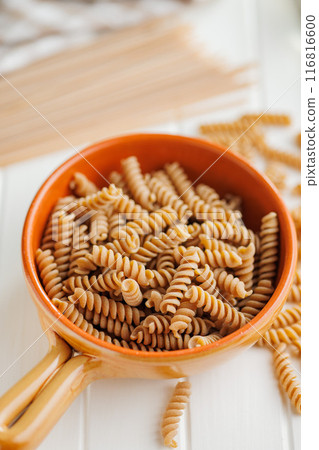Uncooked whole grain pasta. Raw fusilli in bowl. Uncooked whole grain pasta. Raw fusilli in bowl. 116816600