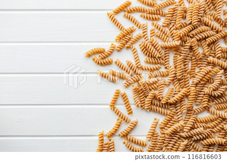 Uncooked whole grain pasta. Raw fusilli pasta on white table. Top view. Uncooked whole grain pasta. Raw fusilli pasta on white table. Top view. 116816603
