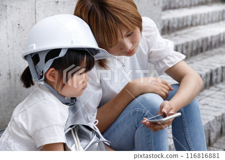 一名戴著頭盔的小學生和她的母親操作智慧型手機。根據防災影像確認安全 116816881