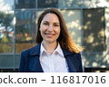 Portrait of a happy caucasian brunette woman in a blue suit stands against the background of a business building and smiles 116817016