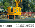 Calgary, Alberta, Canada. Jul 12, 2024. A yellow drilling machine parked on the side of a road with a large, tracked base and a tall, slender tower with a drill bit at the top. 116819535