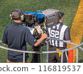 Calgary, Alberta, Canada. Jul 21, 2024. A cameraman films a sports event on the sidelines, accompanied by a referee wearing a striped jersey. 116819537