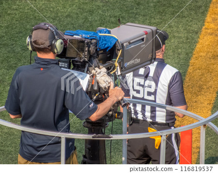 Calgary, Alberta, Canada. Jul 21, 2024. A cameraman films a sports event on the sidelines, accompanied by a referee wearing a striped jersey. 116819537