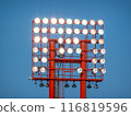A red stadium light tower rises against a clear blue sky. 116819596